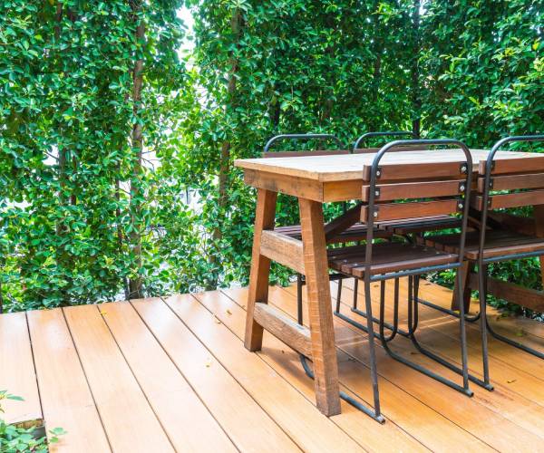 Wood Decking Services patio with wooden table, chairs, and green hedge.